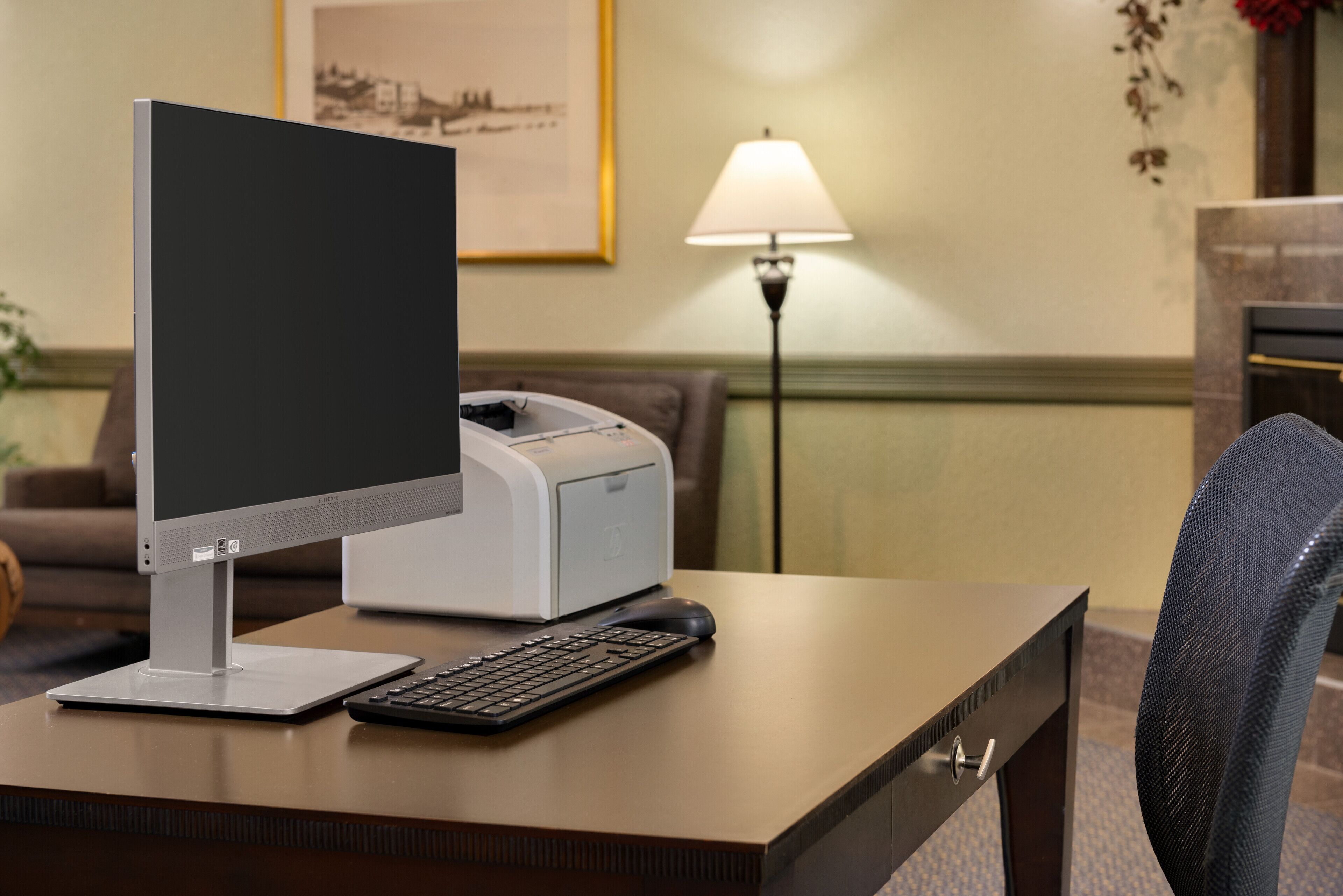 Escritorio de habitación de hotel con una computadora de escritorio, una impresora, un teclado y un ratón.