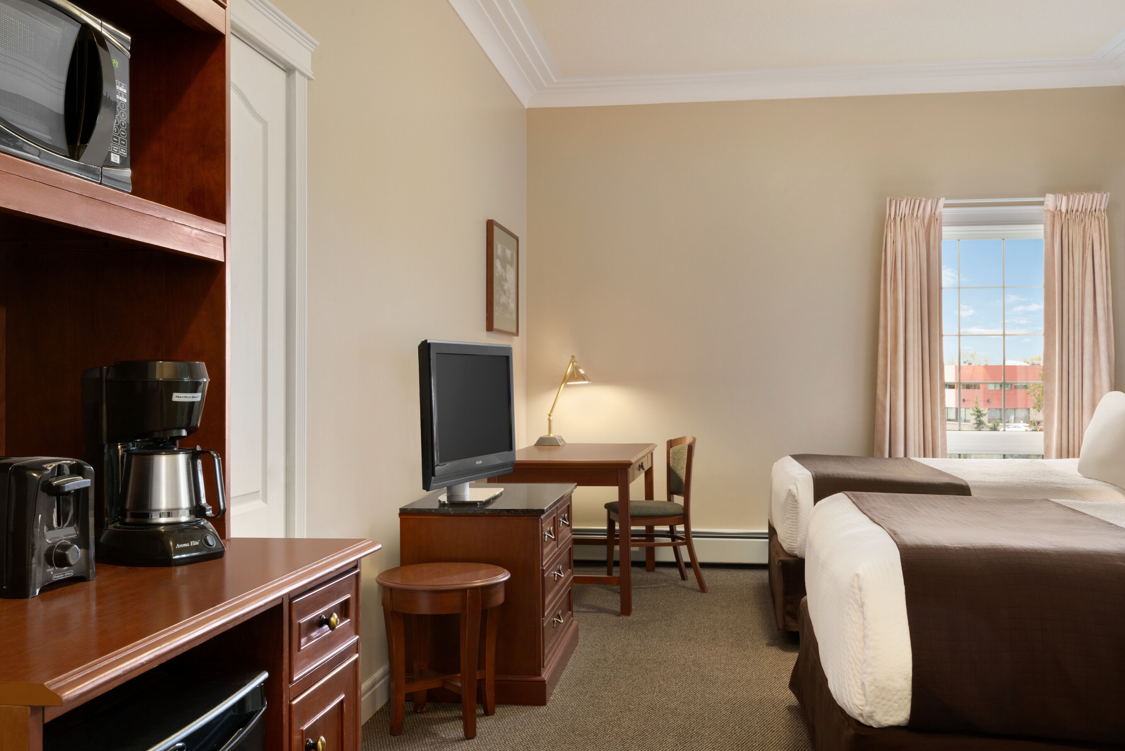 A hotel room with a desk, a television, a coffee maker, a chair, and two beds.