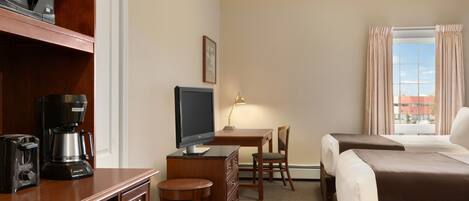 A hotel room with a desk, a television, a coffee maker, a chair, and two beds.