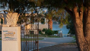 Uma entrada fechada com uma placa para Anthi Maria Apartments, uma palmeira e vista para o mar.