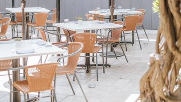 An outdoor patio area with tables and chairs, umbrellas, and a tree.