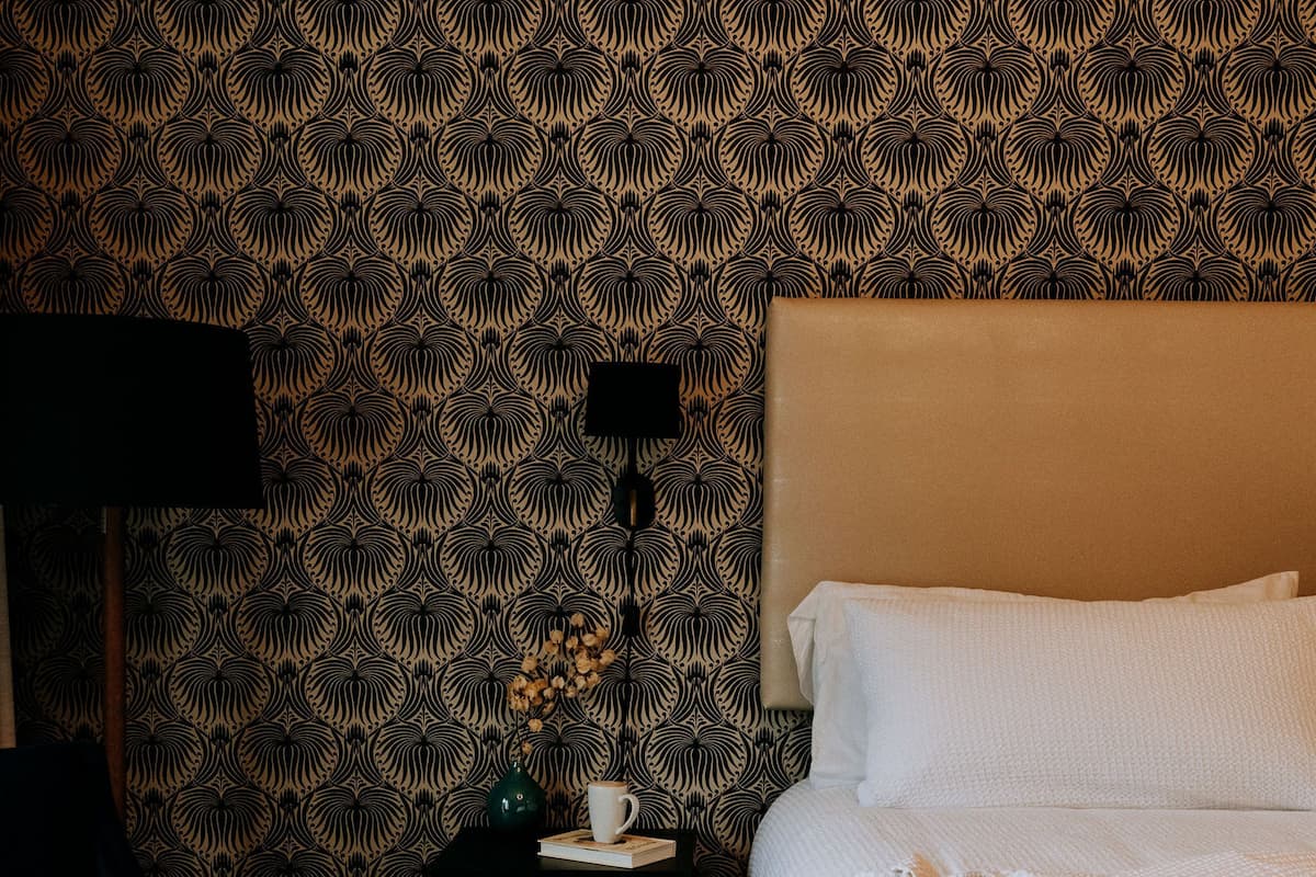 A neatly made bed with white linens, a dark blue chair, a small table with a lamp, and a patterned rug.