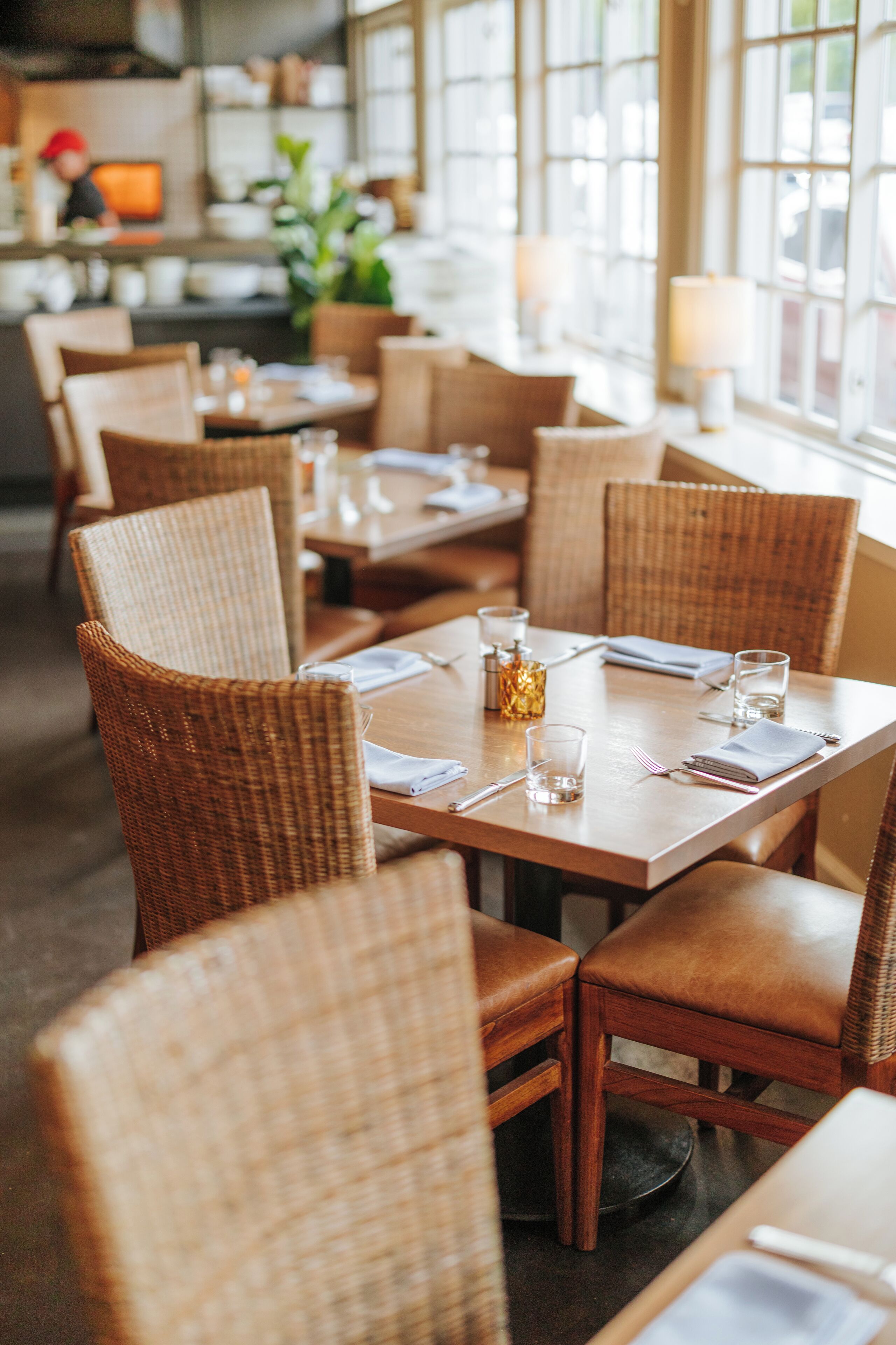 A restaurant with wicker chairs and tables, some with water glasses and napkins.