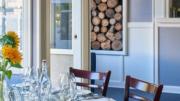 A dining area with a table set for four, a vase with sunflowers, and a stack of logs against the wall.