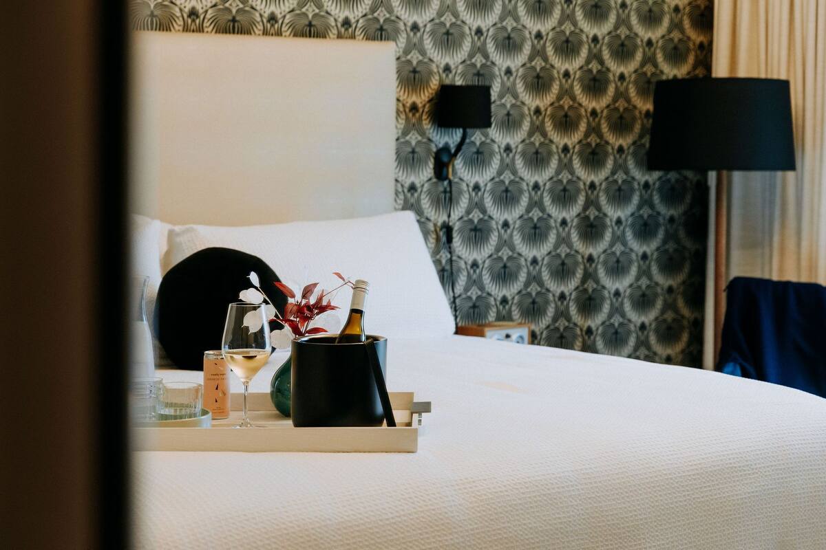 A neatly made bed with a tray of amenities including a bottle, a glass, and a candle.