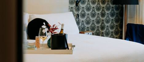 A neatly made bed with a tray of amenities including a bottle, a glass, and a candle.