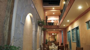 Un interior con paredes de piedra, un balcón con plantas colgantes y una zona de comedor con mesas y sillas.