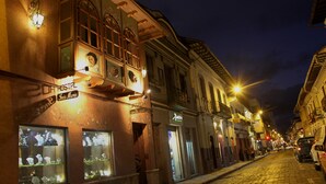 A cobblestone street lined with historic buildings, some with illuminated signs, and a few parked cars.
