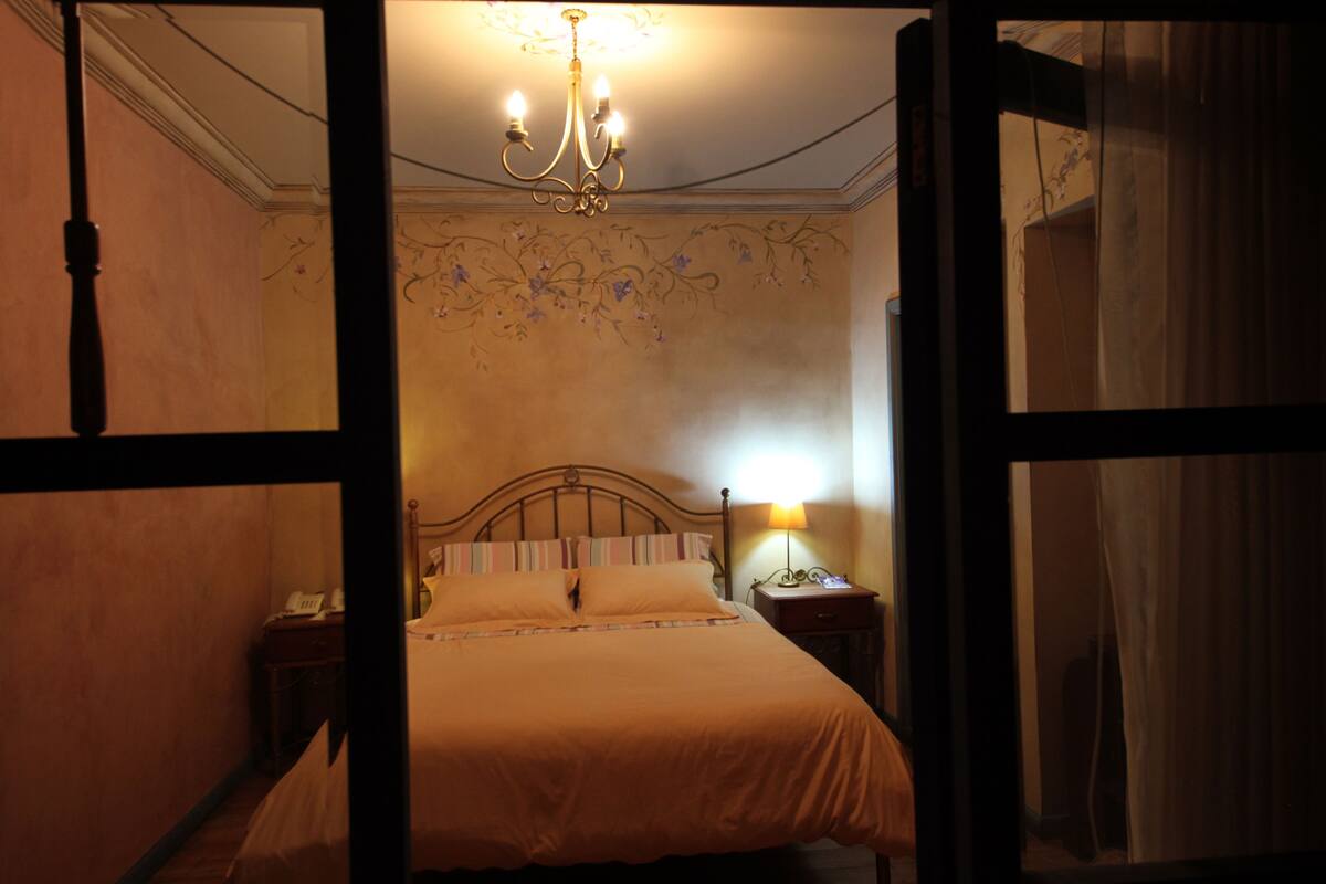 A bedroom with a bed, a nightstand, a lamp, and a chandelier.