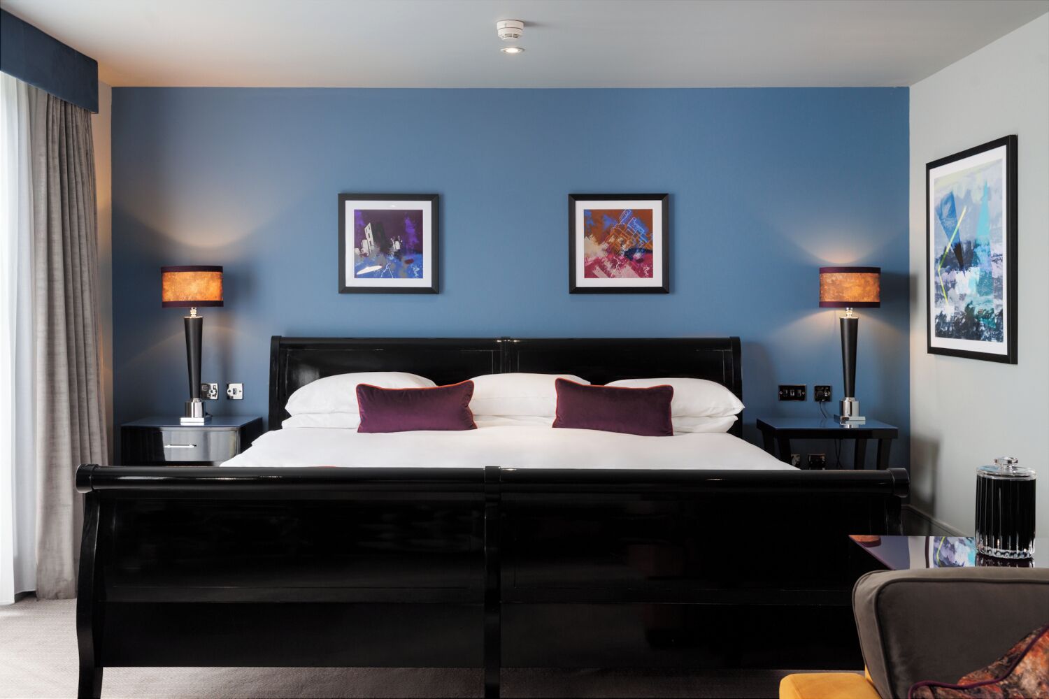 A hotel room with a black four-poster bed, two bedside lamps, a nightstand, and two framed pictures on the wall.