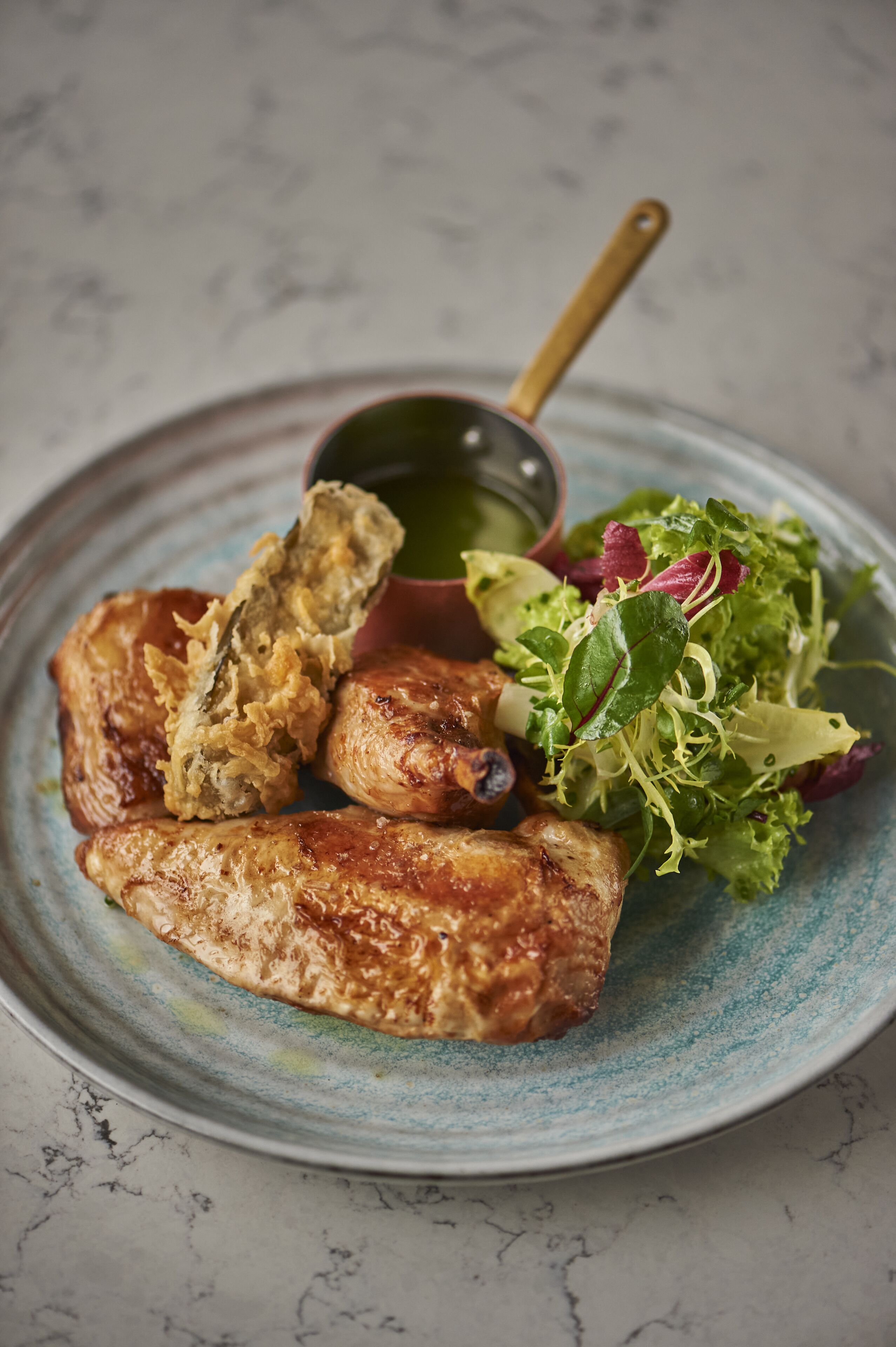 A plate with grilled chicken, a side salad, and a small bowl of sauce.