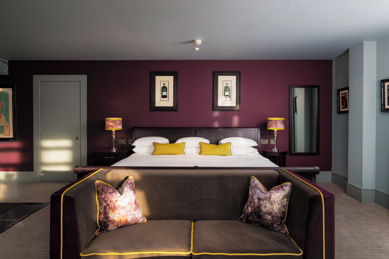 A hotel room with a large bed, two bedside lamps, a sofa with decorative pillows, and framed pictures on the walls.