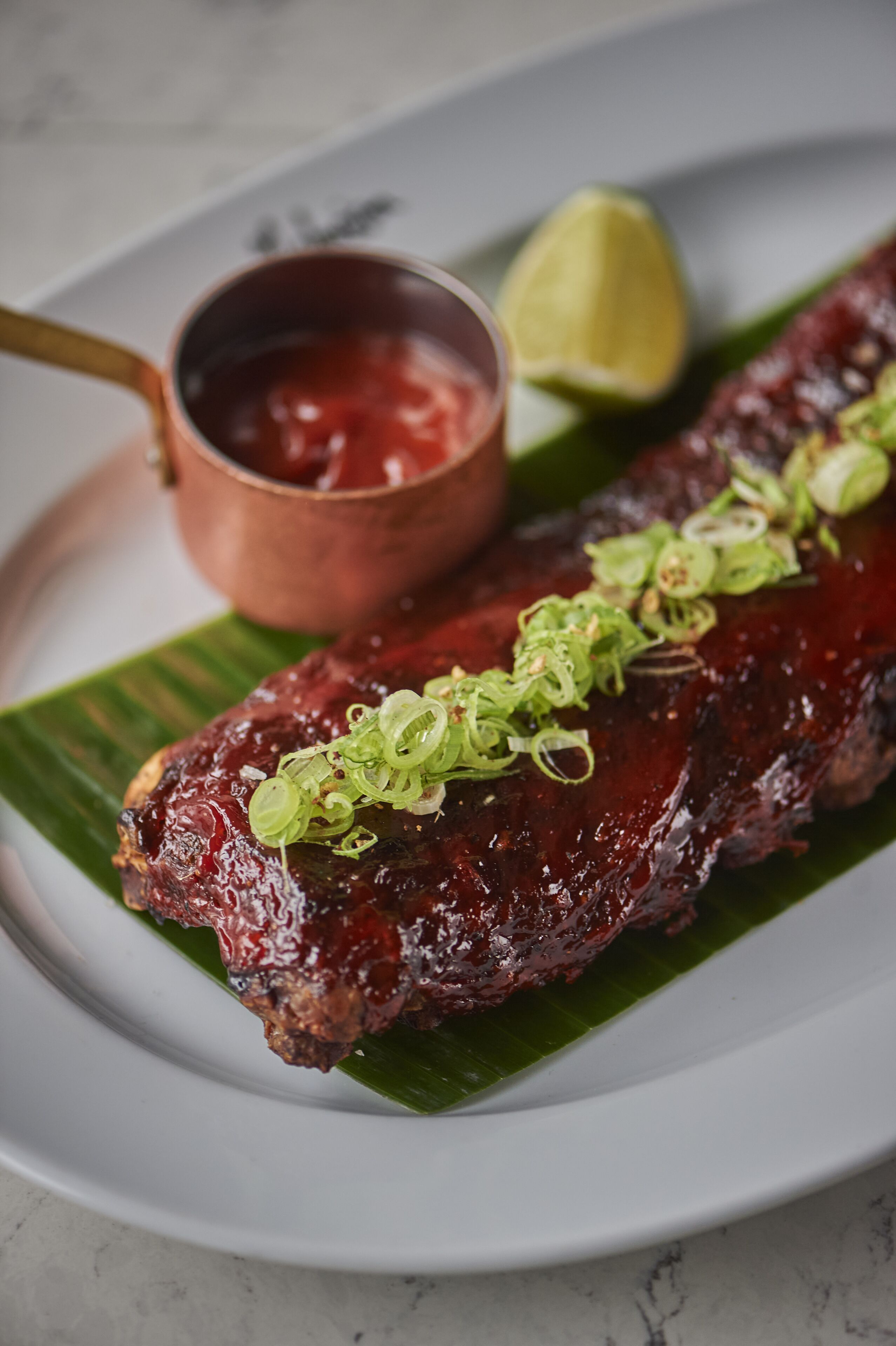 A plate with a grilled meat dish, a small bowl of sauce, and a lime wedge.
