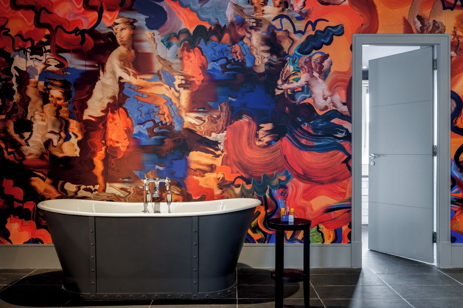 Un baño con un mural grande y colorido en la pared, una bañera independiente y una puerta que da a otra habitación.
