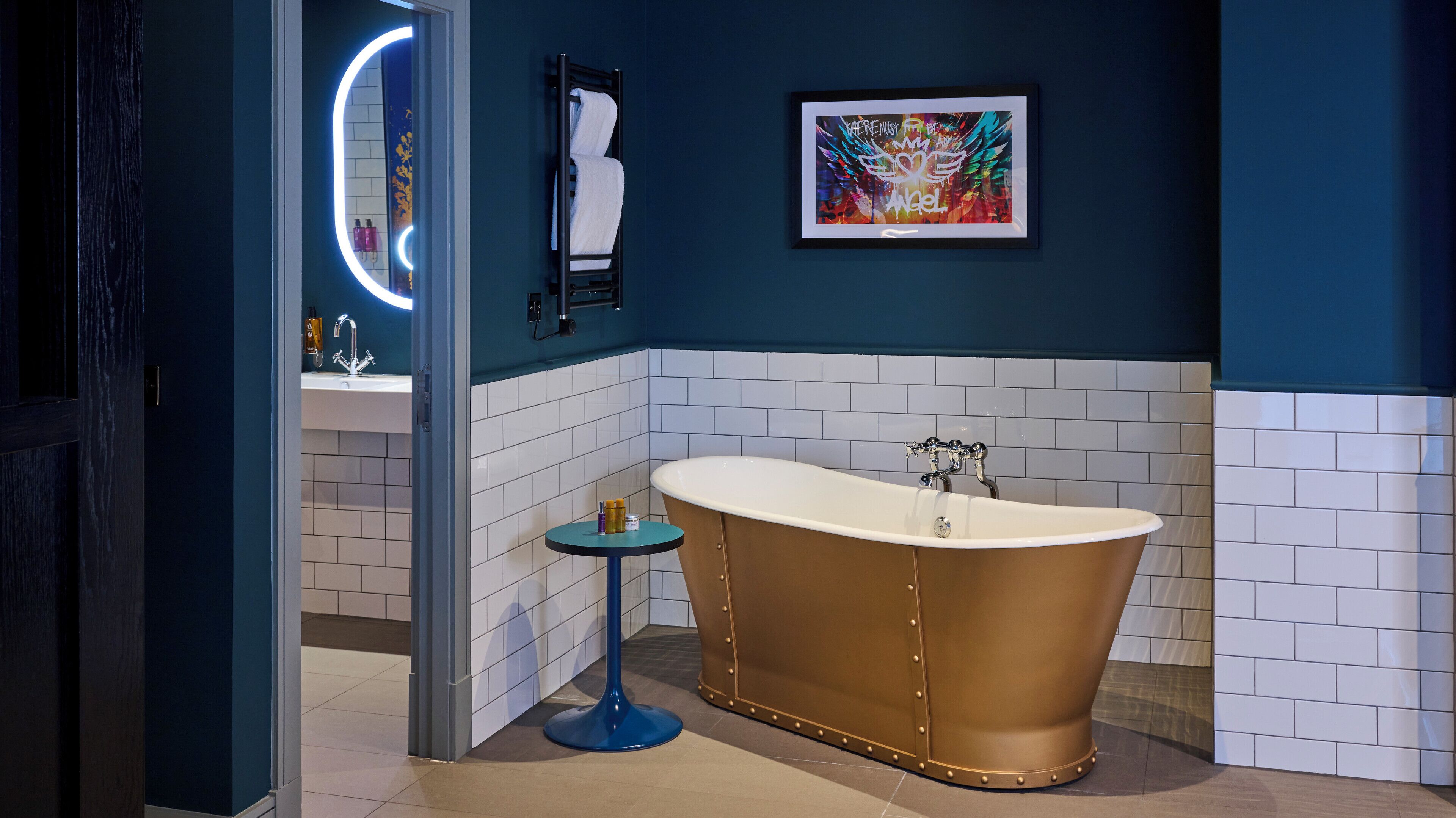A bathroom with a freestanding bathtub, a round blue table, and a framed artwork on the wall.