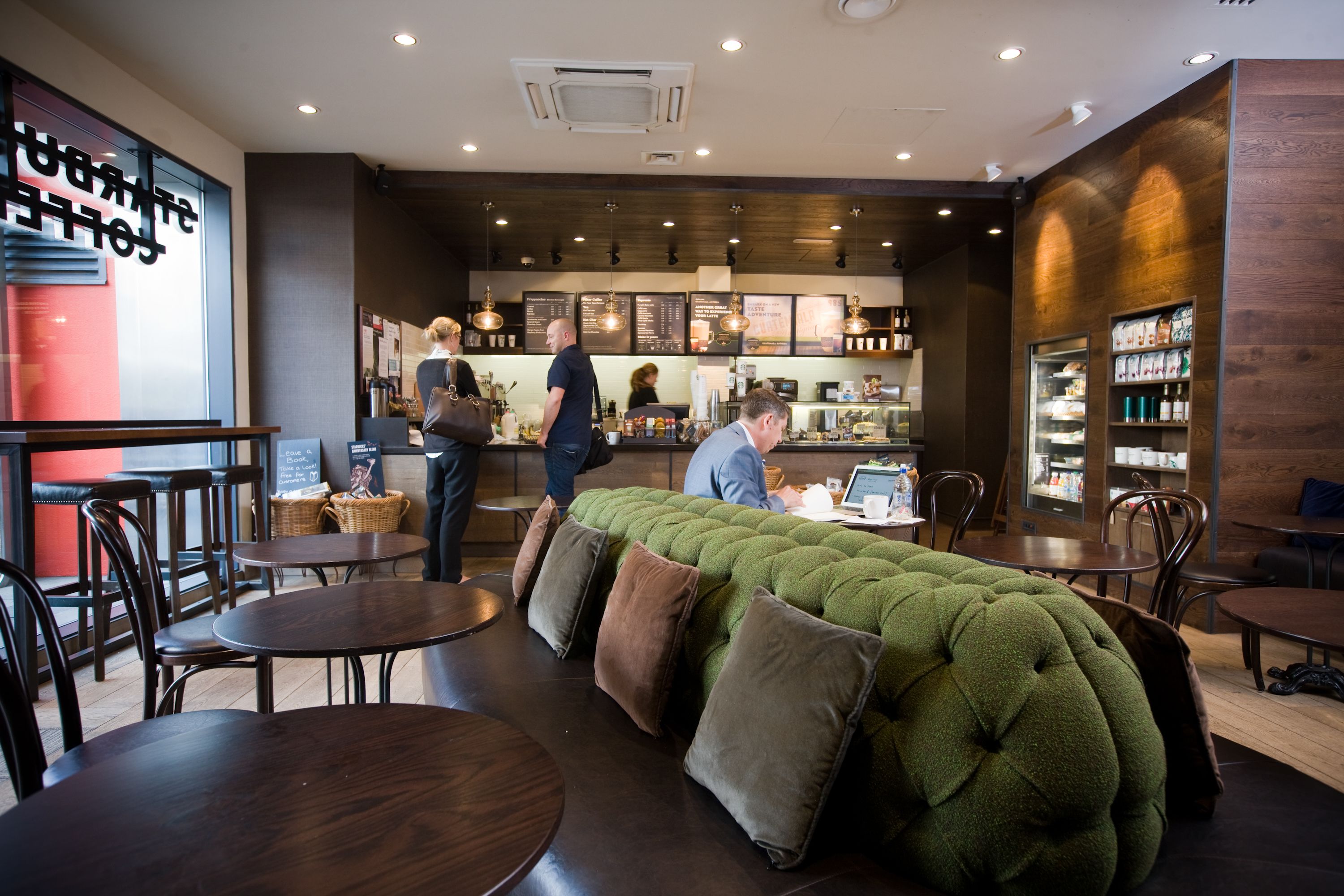 A modern cafe with round tables, a green cushioned seating area, and a menu board in the background.