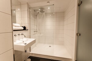 Un baño moderno con ducha de vidrio, lavamanos y espejo.