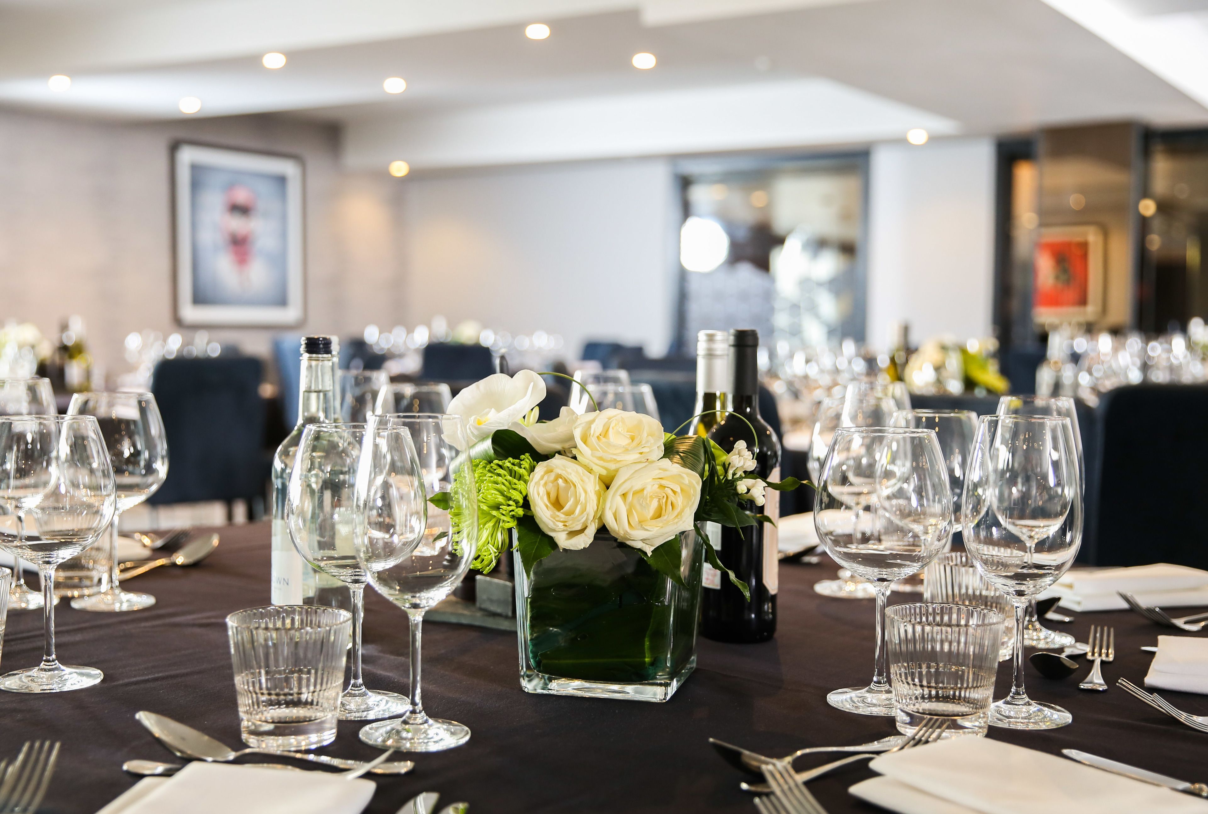 A dining table set with multiple wine glasses, a bottle of white wine, and a vase of white roses.