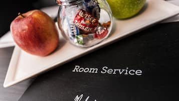 Una mesa con una manzana verde, una botella de té y una manzana roja sobre una bandeja blanca. La bandeja está sobre una superficie negra con el texto "Room Service" y "Malmaison" visible.