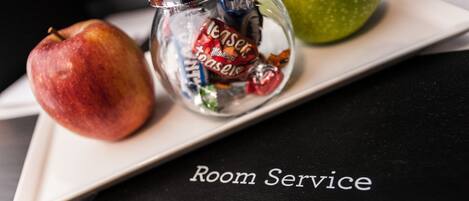 A table with a green apple, a bottle of tea, and a red apple on a white tray. The tray is on a black surface with the text "Room Service" and "Malmaison" visible.