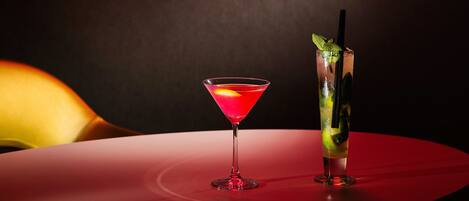 Eine Barbereich mit einem Neon-Lippenschild, einem Martini-Glas und einem hohen Glas mit Trinkhalm und Minze auf einem roten Tisch.
