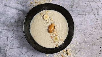 A bowl of oatmeal with almonds and banana slices on a textured surface.