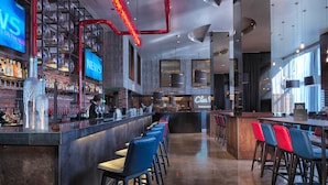 A modern bar area with a bartender, a neon sign, and a variety of bottles and glasses.