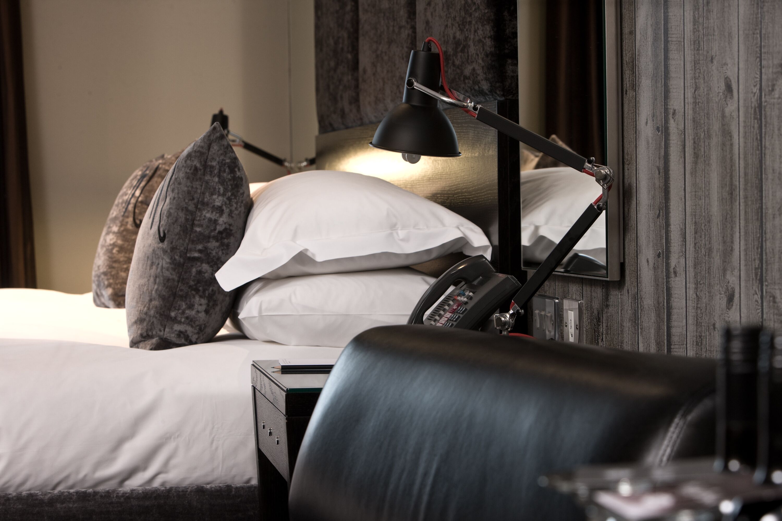 A neatly made bed with white linens, a black desk lamp, and a telephone on the bedside table.