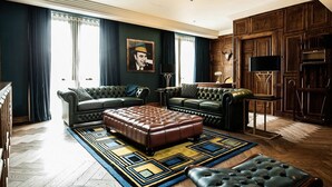 A spacious living room with dark green walls, a large window with curtains, a patterned rug, and a wooden cabinet.