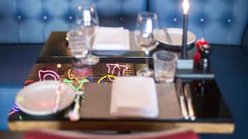 A dining table set with plates, glasses, and a candle, with a neon sign in the background.
