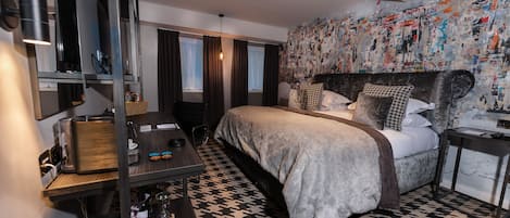 Una habitación de hotel moderna con una cama grande, un escritorio con lámpara, una estantería y una pared decorada con un collage de imágenes.