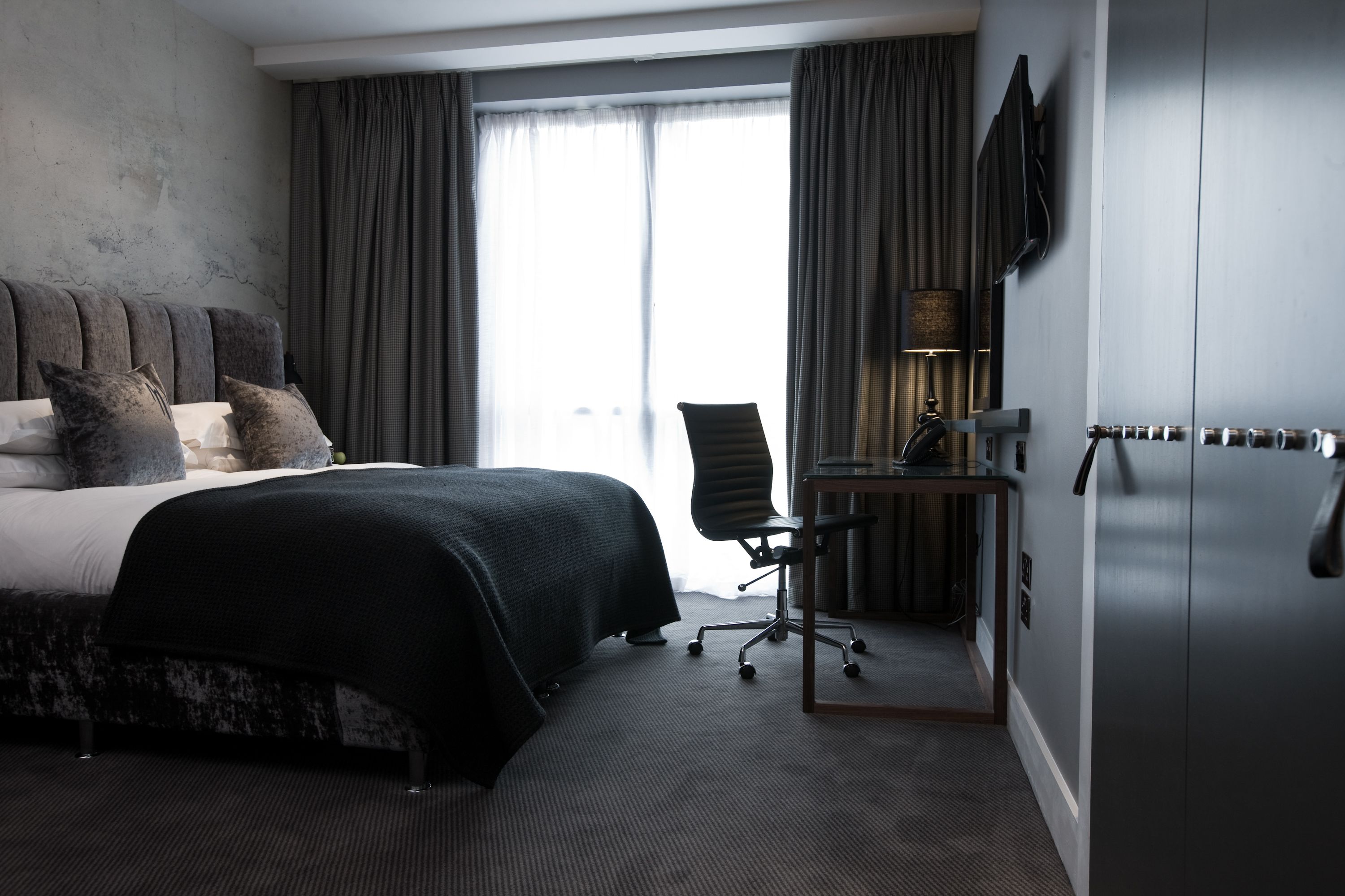 A modern hotel room with a large bed, a desk, and a wardrobe.