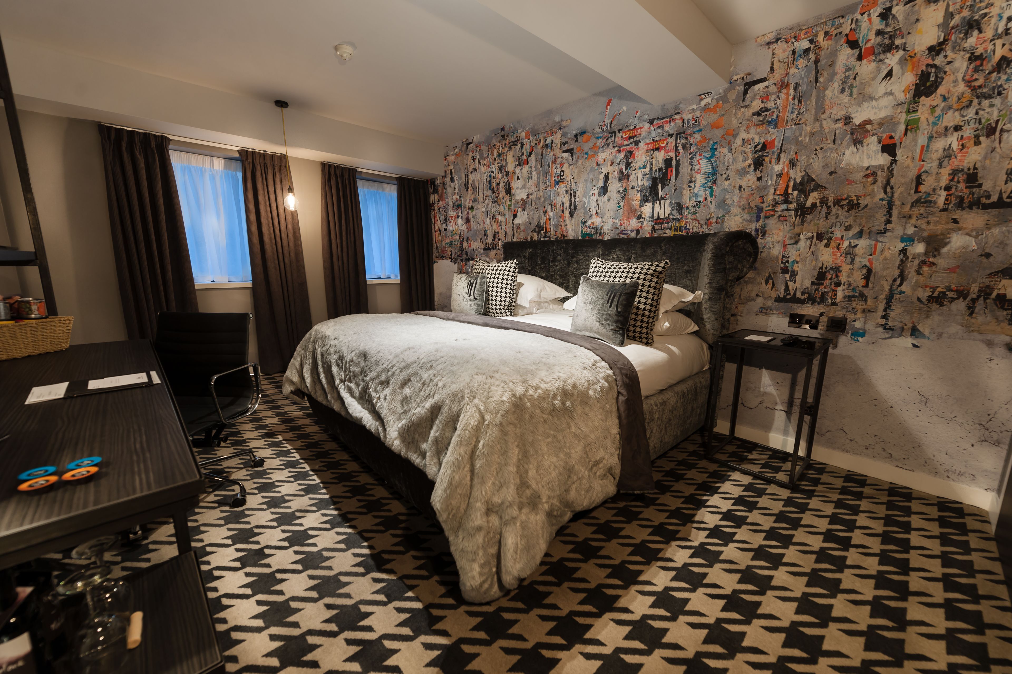 Una habitación de hotel con una cama grande, un escritorio con una silla y una pared decorada con pósters.