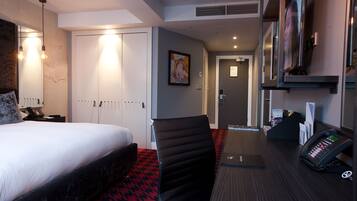 Quarto de hotel com cama, secretária com telefone, uma cadeira e porta para o banheiro.