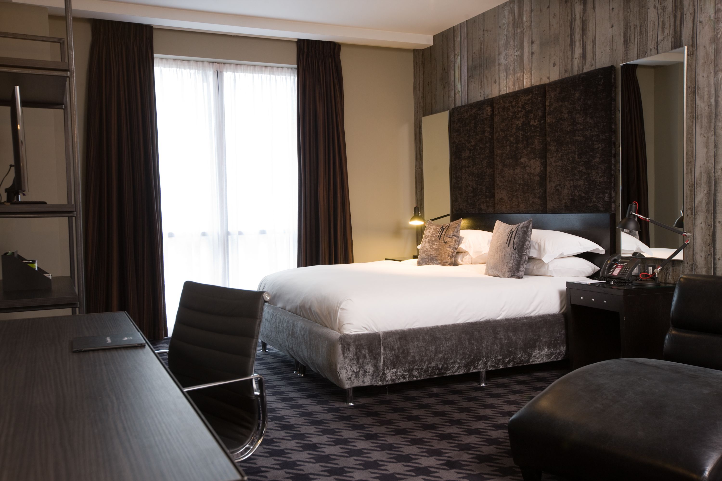 A hotel room with a large bed, a desk, a chair, a desk lamp, and a telephone.