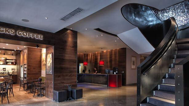 A modern coffee shop interior with a bar area, seating, and a staircase.