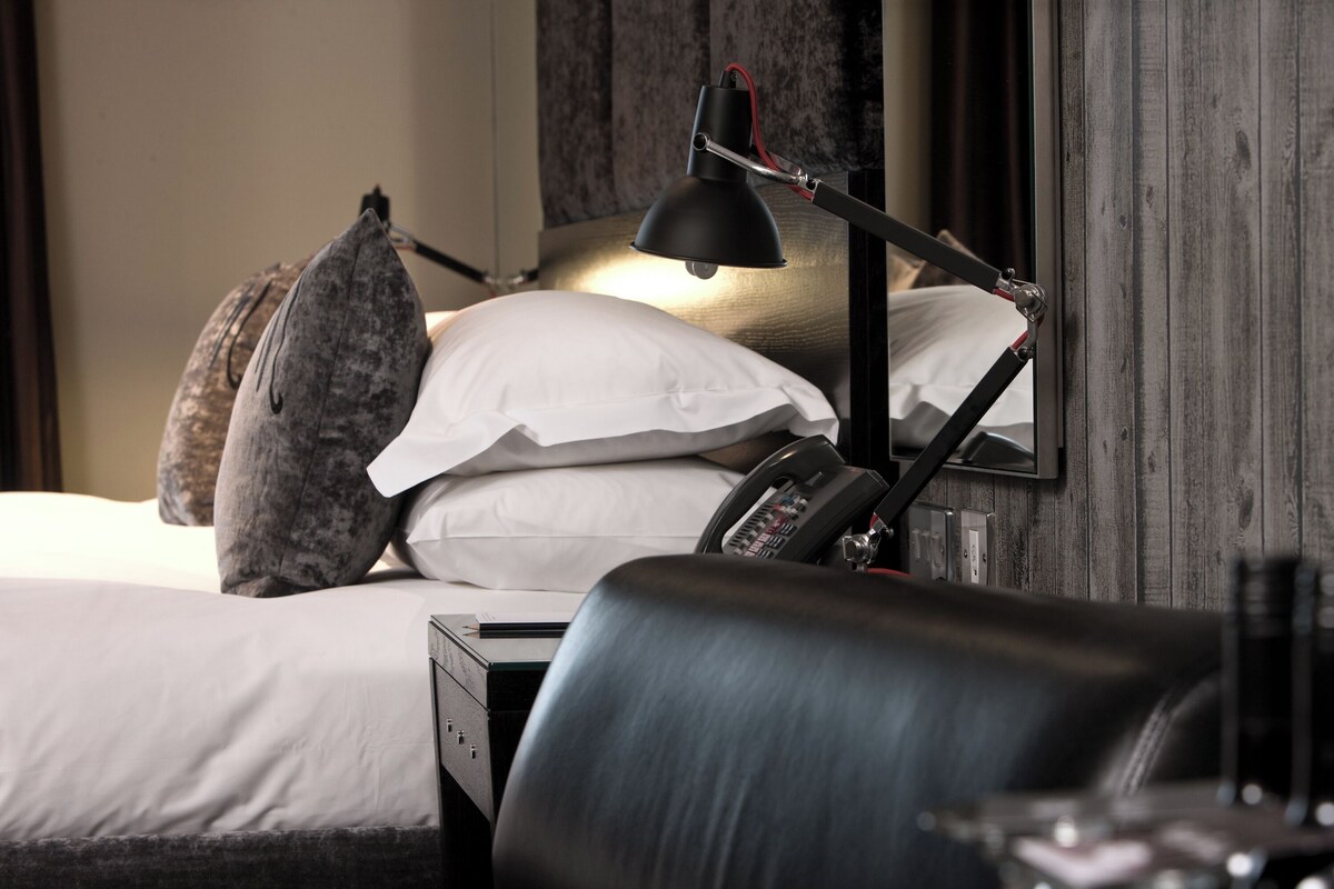 A neatly made bed with white linens, a black desk lamp, and a telephone on the bedside table.