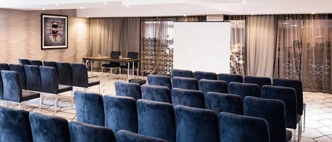 A conference room with rows of blue chairs, a whiteboard, and a table with chairs.