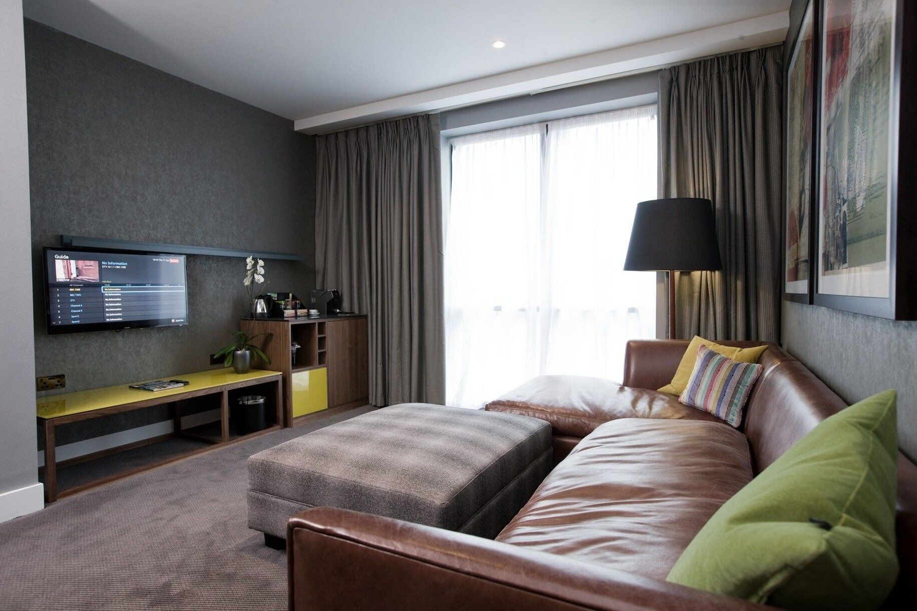 Una habitación de hotel moderna con una cama grande, un escritorio con una computadora y un televisor montado en la pared.