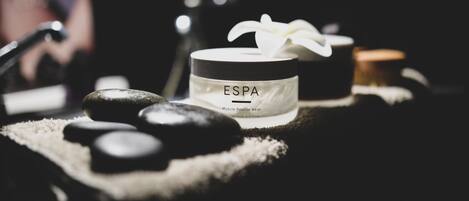 A spa setting with a jar labeled "ESPA Muscle Rescue Balm" and a white flower on top.