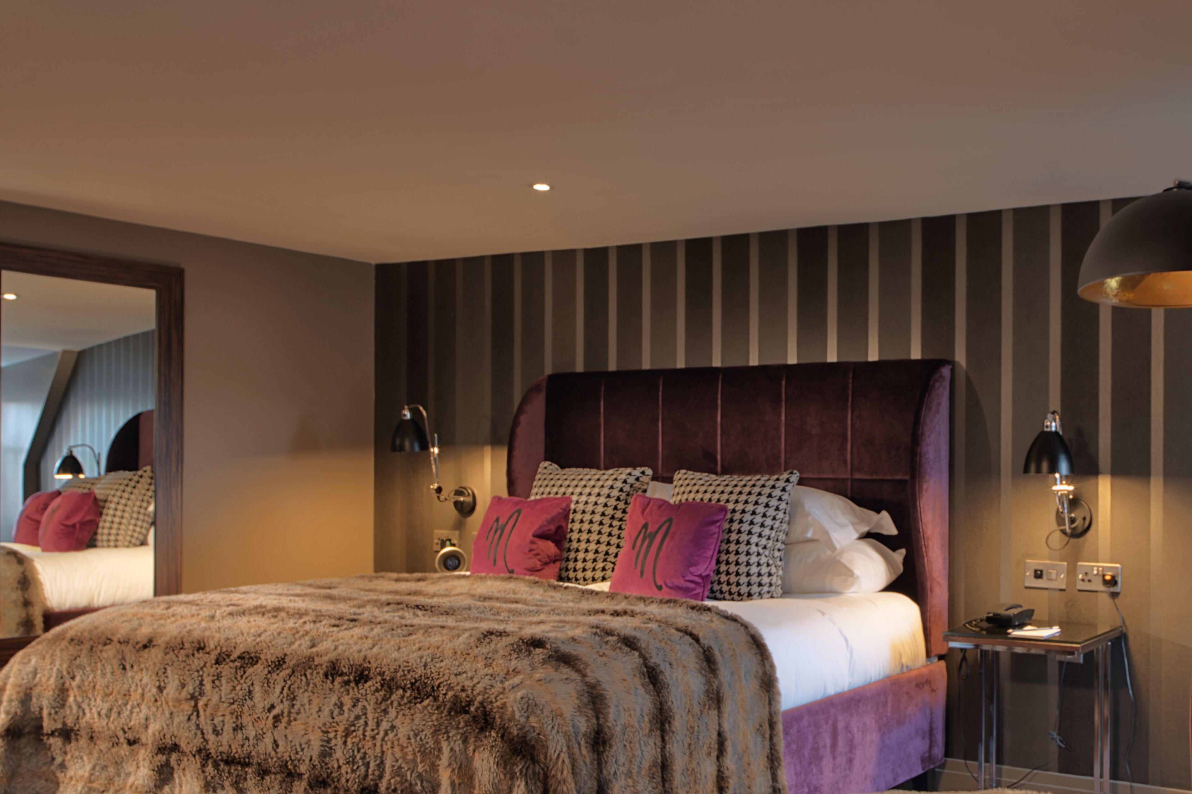 A modern bedroom with a large bed, striped wallpaper, and a mirror.