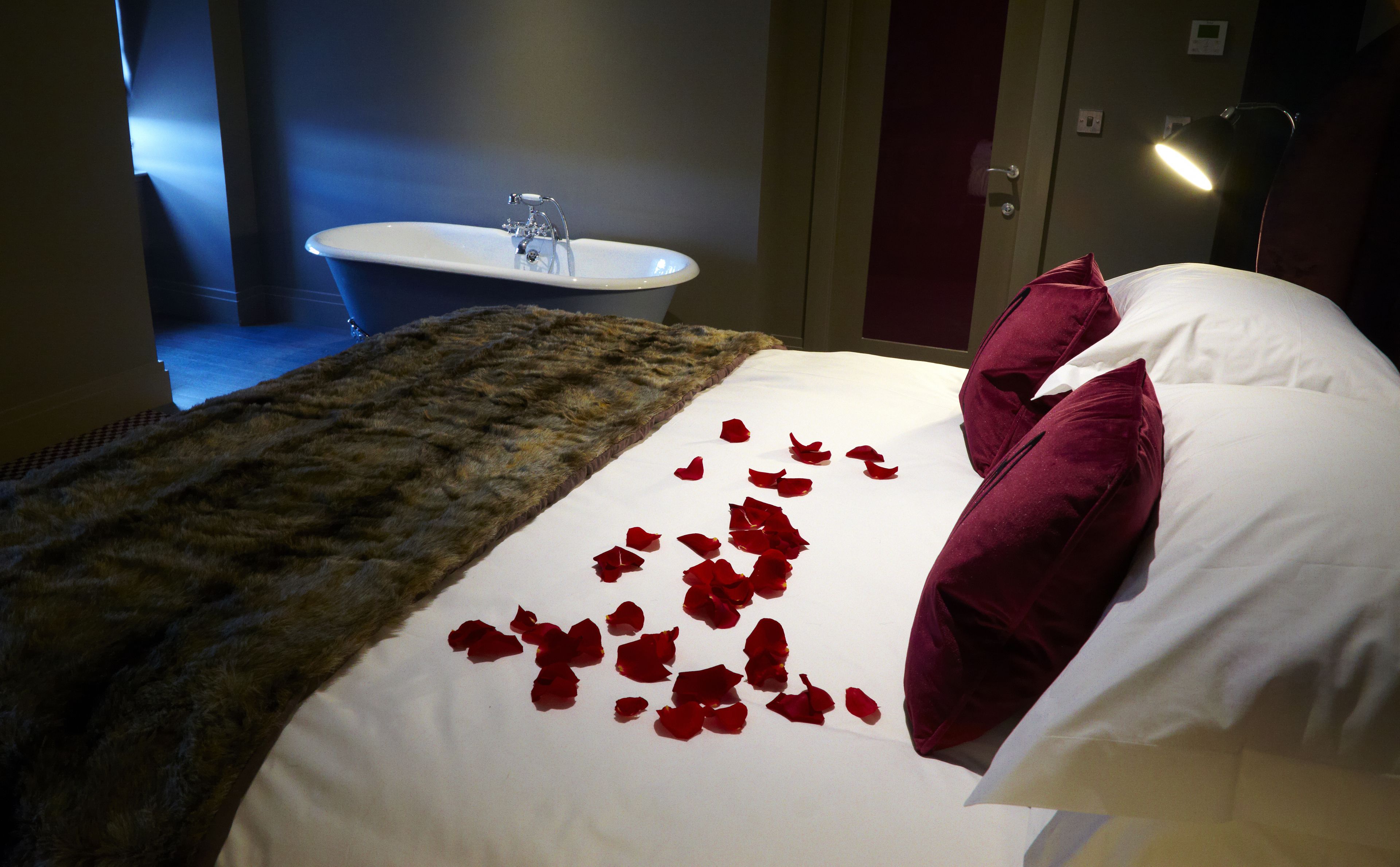 Une chambre d’hôtel avec un lit, une baignoire blanche et un plaid en fourrure.