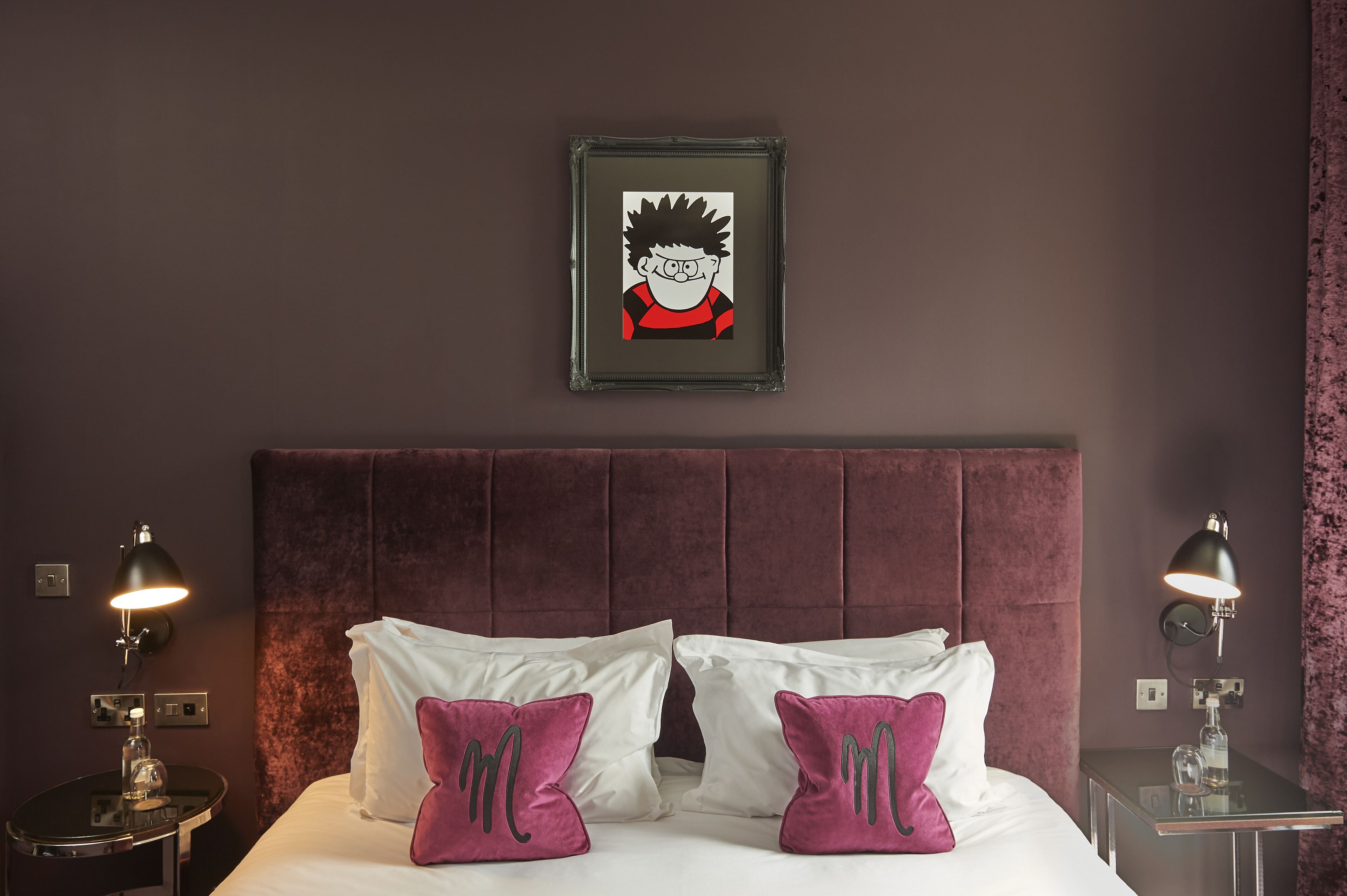 Een hotelkamer met een groot bed, twee bedlampen, een ingelijst schilderij aan de muur en een nachtkastje met een lamp.
