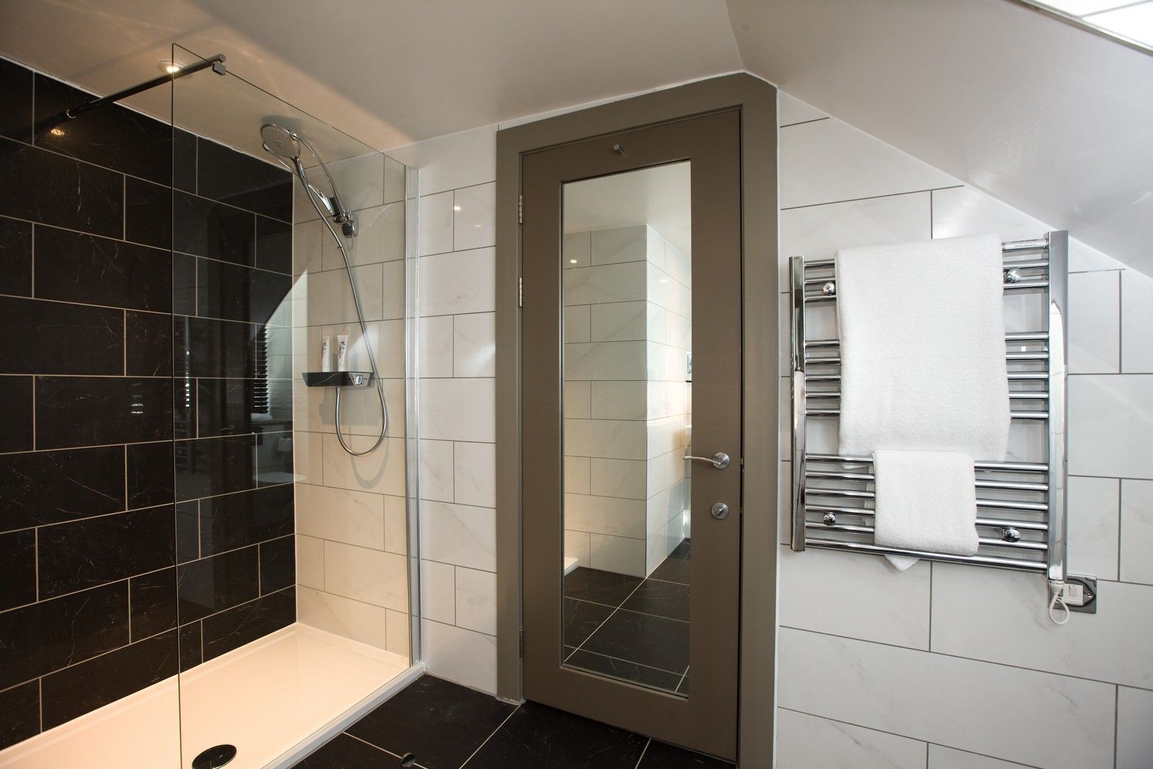A modern bathroom with a glass shower enclosure, a white bathtub, and a towel rack with towels.