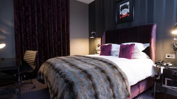 A hotel room with a large bed, a desk, a chair, a lamp, and a framed picture on the wall.