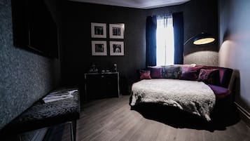 Une chambre à coucher avec un lit, un bureau, une chaise, une lampe et une fenêtre avec des rideaux.