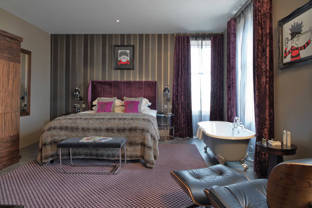 Ein Schlafzimmer mit einem großen Bett, einer Sitzecke mit einem Sessel, einem Schminktisch mit Spiegel und einer Badewanne.