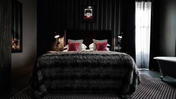 A modern bedroom with a large bed, a headboard with a framed picture, and a bathtub.