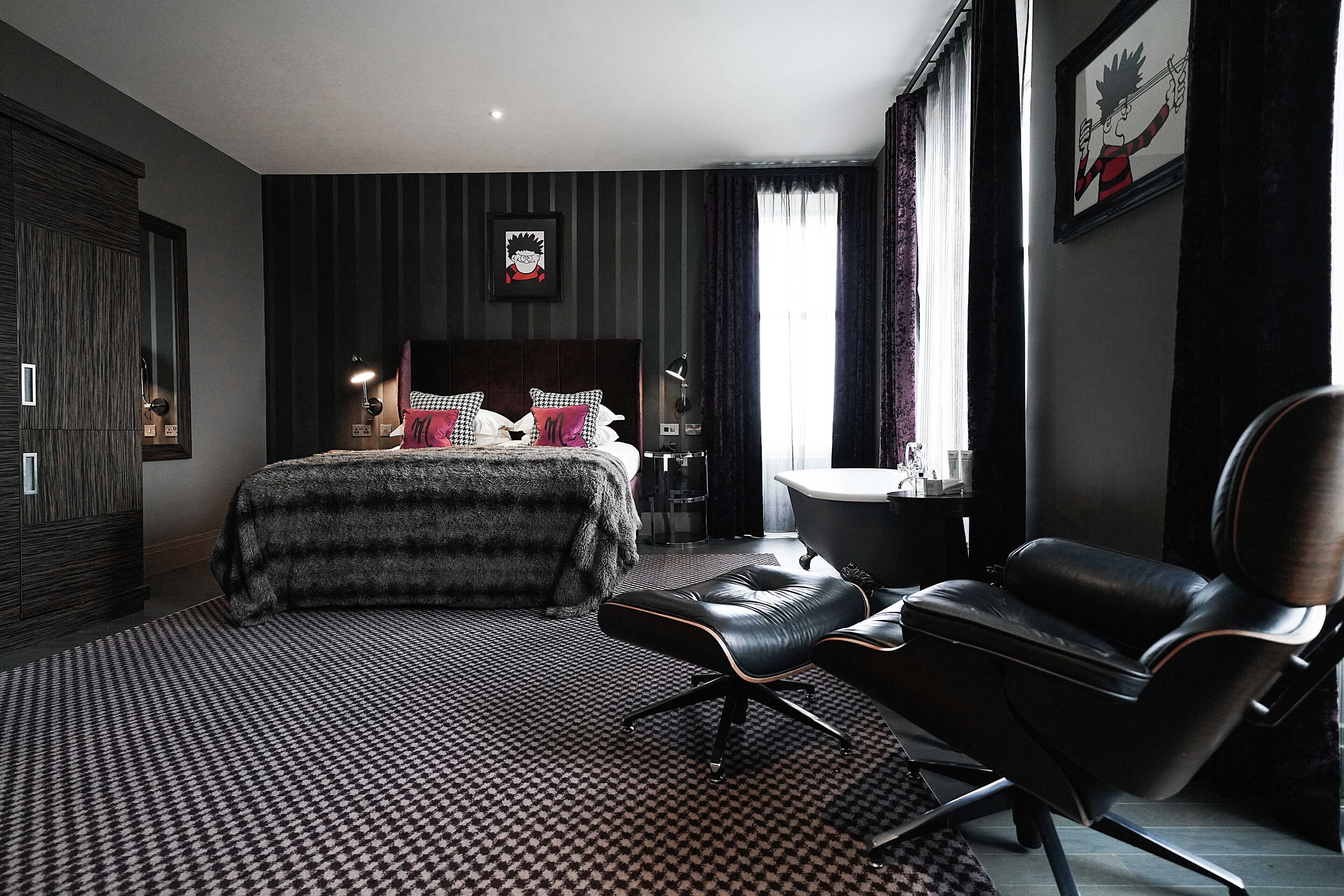 Ein modernes Schlafzimmer mit einem großen Bett, einem schwarzen Ledersessel und einem Badezimmer mit einer Badewanne.