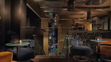 A bar area with round tables, cushioned chairs, and a staircase leading to a lower level.